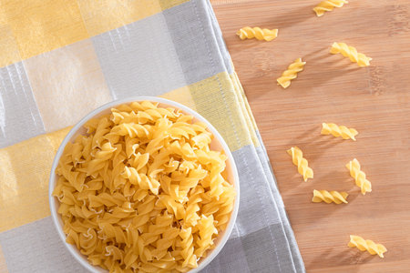 Uncooked Fusilli Pasta in White Bowl on Wooden Board. Raw and Dry Macaroni. Unhealthy and Fat Food. Italian Cultureの写真素材