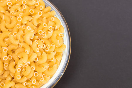 Uncooked Chifferi Rigati Pasta in Glass Jar on Black Background. Fat and Unhealthy Food. Classic Dry Macaroni. Italian Culture and Cuisine. Raw Pastaの写真素材
