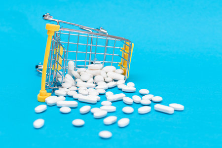 Buying Medicines. Expensive Medicine and Inflation: Scattered Pills or Capsules and Shopping Cart on Blue Background. Global Pharmaceutical Industry and Big Pharma. Ordering Pharmaceutical Productsの写真素材