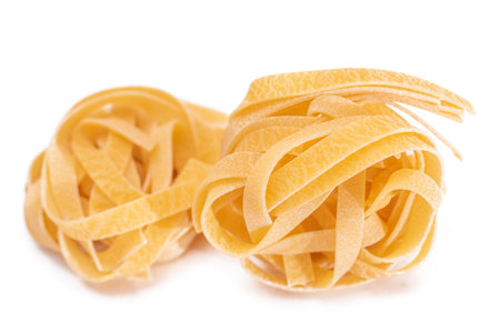 Two Classic Italian Raw Egg Fettuccine - Isolated on White Background. Dry Twisted Uncooked Pasta. Italian Culture and Cuisine. Raw Golden Macaroni Pattern - Isolationの写真素材