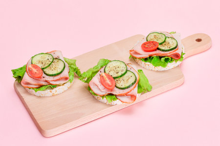 Light Breakfast. Quick and Healthy Sandwiches. Rice Cakes with Ham, Tomato, Fresh Cucumber and Green Salad on Wooden Cutting Boardの写真素材