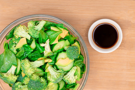Fresh Green Salad of Avocado, Broccoli, Spinach and Cucumber for Detox with Soy Sauce on Wooden Cutting Board. Vegan Salad. Vegetarian Culture. Raw Food. Healthy Eating and Vegetable Dietの写真素材
