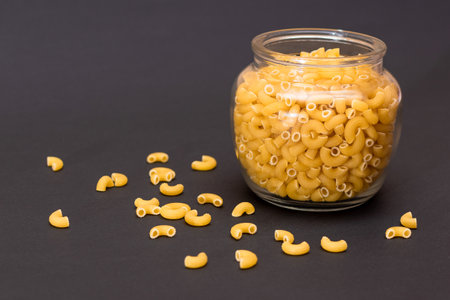 Uncooked Chifferi Rigati Pasta in Glass Jar on Black Background. Scattered Classic Dry Macaroni. Italian Culture and Cuisine. Raw Pastaの写真素材