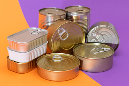 A Group of Stacked Tin Cans with Blank Edges on Split Orange and Violet Background. Canned Food....