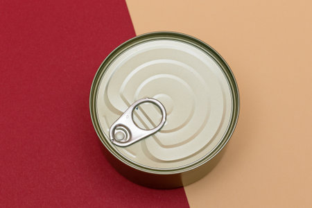 Unopened Tin Can with Blank Edge on Split Red and Beige Background. Canned Food. Aluminum Can for...