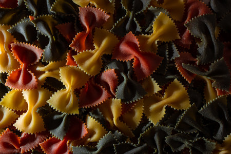 Uncooked Vibrant Colored Farfalle Pasta: A Culinary Canvas of Multicolored Bow-Tie Macaroni, Creating a Lively and Textured Background for Gourmet Cooking Enthusiasts. Colored Dry Pasta. Raw Macaroniの写真素材