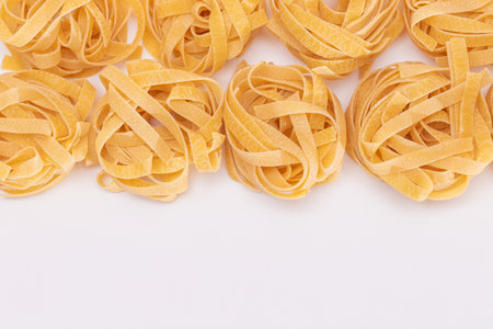 Classic Italian Raw Egg Fettuccine with Copy Spase on White Background. Dry Twisted Uncooked Pasta. Italian Culture and Cuisine. Raw Golden Macaroni Patternの写真素材