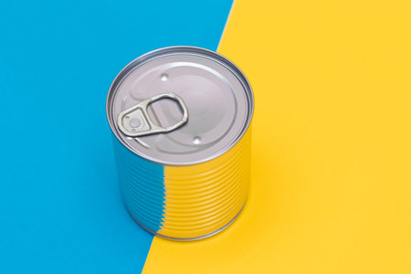 Tin Can on Split Blue and Yellow Background. Canned Food. Aluminum Can for Safe and Long Term...
