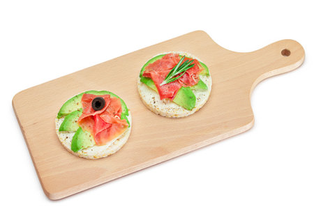Rice Cake Sandwich with Avocado, Jamon, Olives and Rosemary on Wooden Cutting Board - Isolated on White. Easy Breakfast. Quick and Healthy Sandwiches. Crispbread with Tasty Filling - Isolationの写真素材