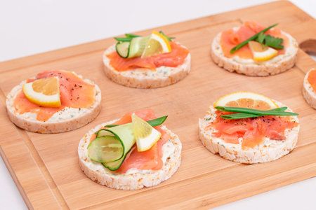 Rice Cake Sandwiches with Fresh Salmon, Cucumber, Lemon and Greens on Bamboo Cutting Board. Quick and Healthy Sandwiches. Crispbread with Fresh Fillings.の写真素材