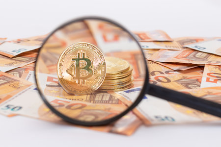 A Stack of Bitcoin Coins Visible Through a Magnifying Glass on the 50-Euro Banknotes. Euro Currency and Crypto Currency. Orange Paper Money. A Lot of Fifty-Euro Bills. Anonymous Payments Conceptの写真素材