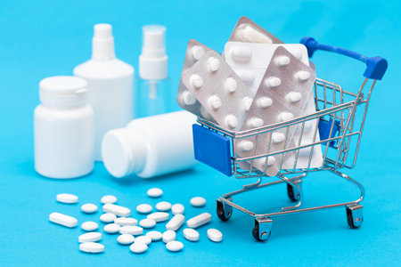 Expensive Medicine and Inflation Concept: Pills and Capsules in Shopping Cart on Blue Background. Global Pharmaceutical Industry and Big Pharma. Ordering Pharmaceutical Productsの写真素材