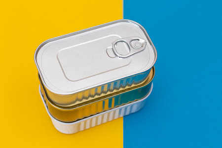 A Group of Stacked Tin Cans on Split Blue and Yellow Background. Canned Food. Aluminum Cans for Safe...
