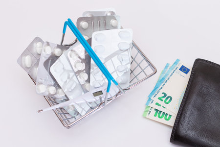 Expensive Medicine and Inflation Concept: Pills and Capsules in a Shopping Basket and Black Wallet with Euro Money on White Table. Global Pharmaceutical Industry and Big Pharma. Trade in Medicinesの写真素材