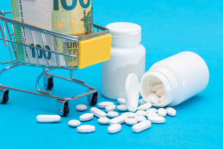 Buying Medicines. Expensive Medicine and Inflation: Scattered Pills or Capsules and Shopping Cart on Blue Background. Global Pharmaceutical Industry and Big Pharma. Ordering Pharmaceutical Productsの写真素材