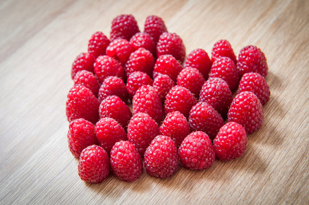 Raspberry heart. Valentines day background. Fresh raspberries from village garden. Love berries symbol on wooden texture.の写真素材