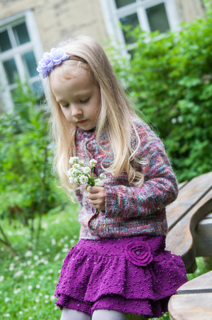 little beautiful girl with long blond hair is smelling flowers in natureの写真素材