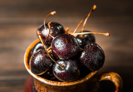 Ripe sweet cherry berries with drops in a brown earthenware plate on a wooden surface background.の写真素材
