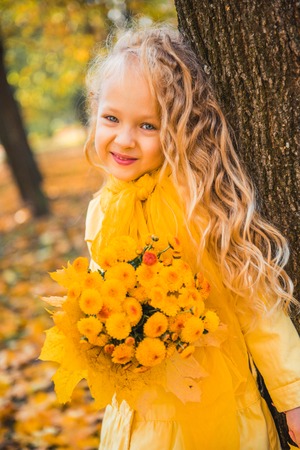 Little girl with blond hair in autumn background with yellow flowersの写真素材