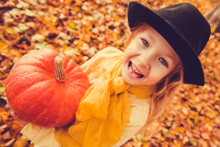Little beautiful girl with blond hair with big pumpkin in autumn background. Halloweenの写真素材