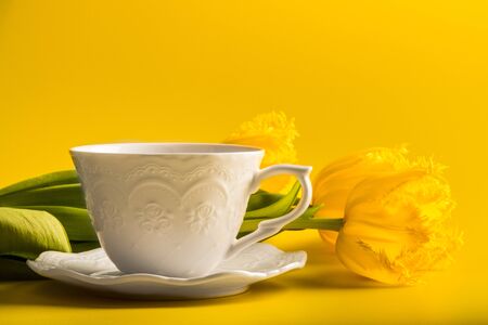 Yellow tulips with cup of tea or coffee on yellowの写真素材