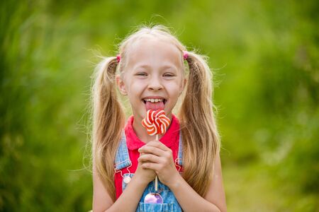 Blonde little girl with long hair and candy on a stickの写真素材
