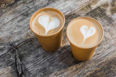 Two paper cups of coffee with heart shape latte art on yellow backgroundの写真素材