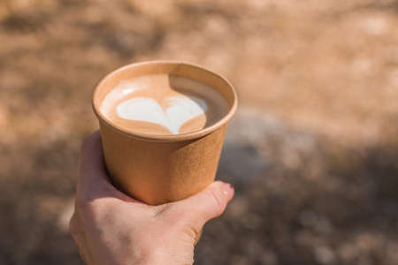 Paper cup of coffee is holding on hand on nature backgroundの写真素材
