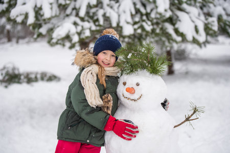 Happy child girl plaing with a snowman on a snowy winter walkの写真素材
