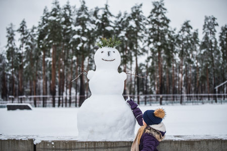 Happy child girl plaing with a snowman on a snowy winter walkの写真素材