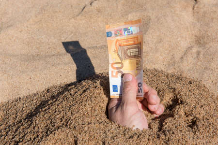Fifty euros in the hand of a man sticking out of the sand. Concept finance money holiday relax vacation.の写真素材
