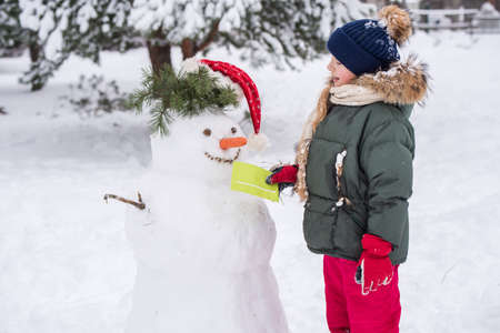 Happy blonde cute child girl gives a letter to a snowmanの写真素材