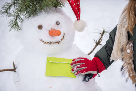 Child girl gives a letter to a snowman on a snowy winter walkの写真素材