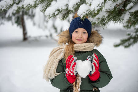 Happy child girl plaing with snow with heart made of snow.の写真素材