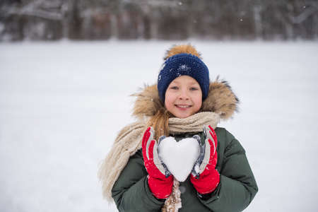 Happy child girl plaing with snow with heart made of snow.