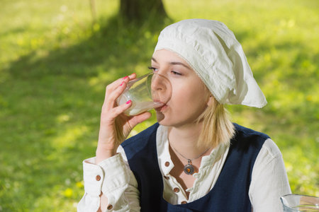 Latvian woman in traditional clothing with milk glass on natureの写真素材