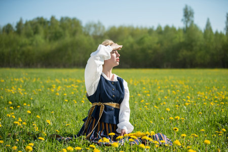 Young woman in national clothes wearing yellow dandelion wreath in spring field. Springtime