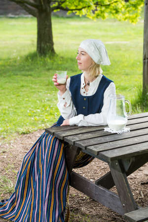 Latvian woman in traditional clothing with milk glass on natureの写真素材