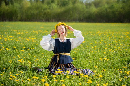 Young woman in national clothes wearing yellow dandelion wreath in spring field. Springtimeの写真素材
