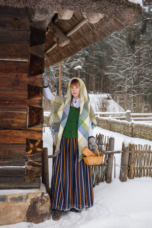 Latvian woman in traditional ethnic clothing posing on nature winter background in village. Riga Latviaの写真素材