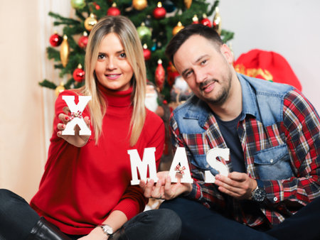 Couple sitting on the sofa and holding wooden letters Xmas.