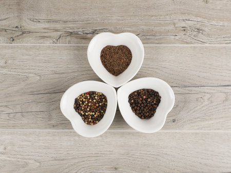 Heart shaped bowls filled with different spices on a wooden background, top view