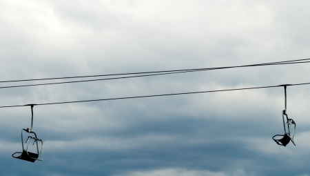 Two empty ski lift chairs hanging on steel cable against overcast sky の写真素材