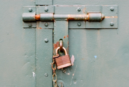 Closed rusted padlock blocking deadbolt on green steel door の写真素材