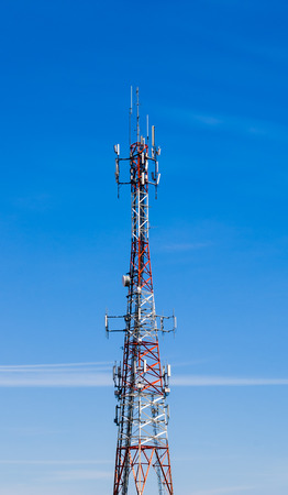 Large red and white communications tower on blue sky 