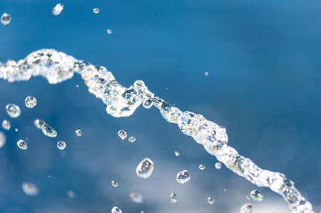 Abstract close-up of illuminated water stream falling into focus against blurred blue background.の写真素材