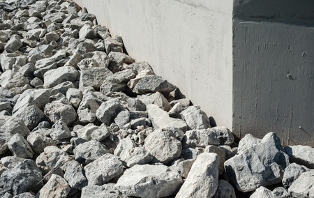 Uneven rock and gravel rubble by smooth gray concrete wall corner.の写真素材