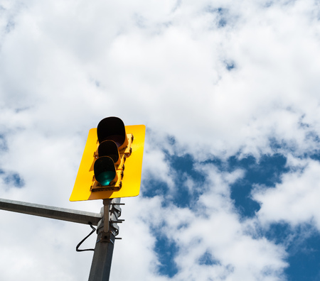 Traffic signal on metal pole with green light lit in yellow structure against partly cloudy sky.の写真素材