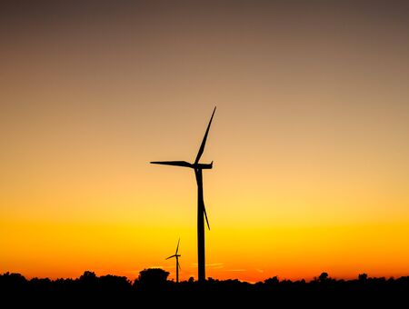 Black silhouette of wind turbines against orange sky at dusk.