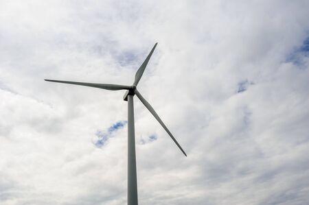 Single wind turbine against cloudy sky.